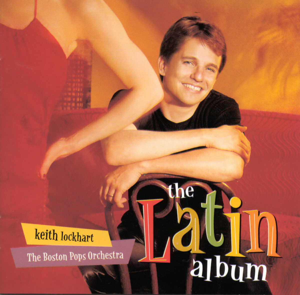 Latin Album cover depicts Keith Lockhart dressed in black slacks and short-sleeved t-shirt sitting on a chair backwards while a woman dressed in red partially covers the left foreground of frame