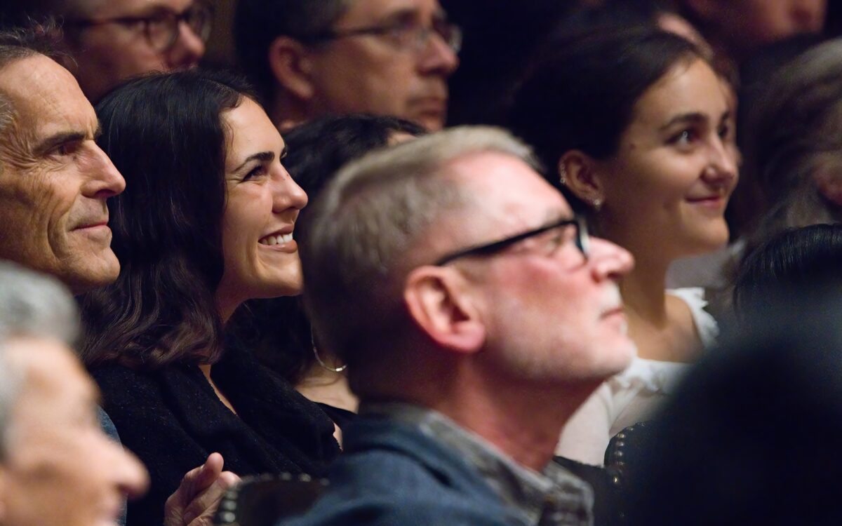 Audience members smiling in symphony hall looking up to the stage.