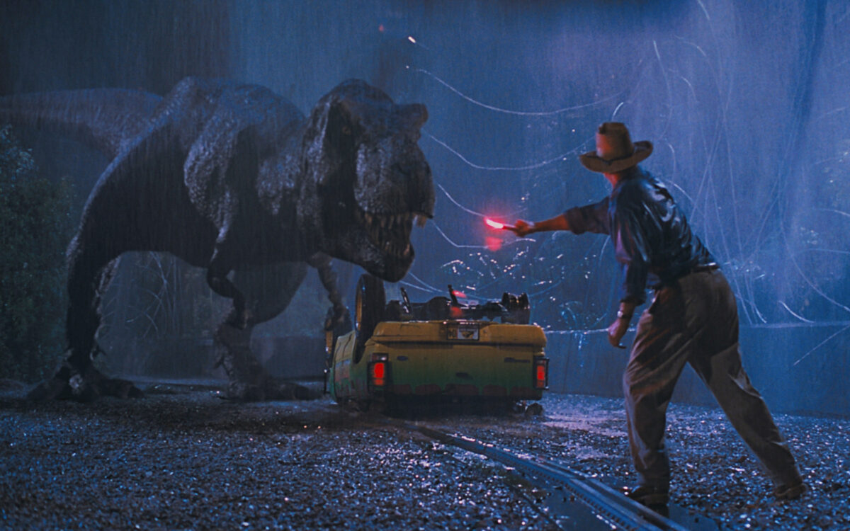 A dinosaur approaches a man waving a red flare
