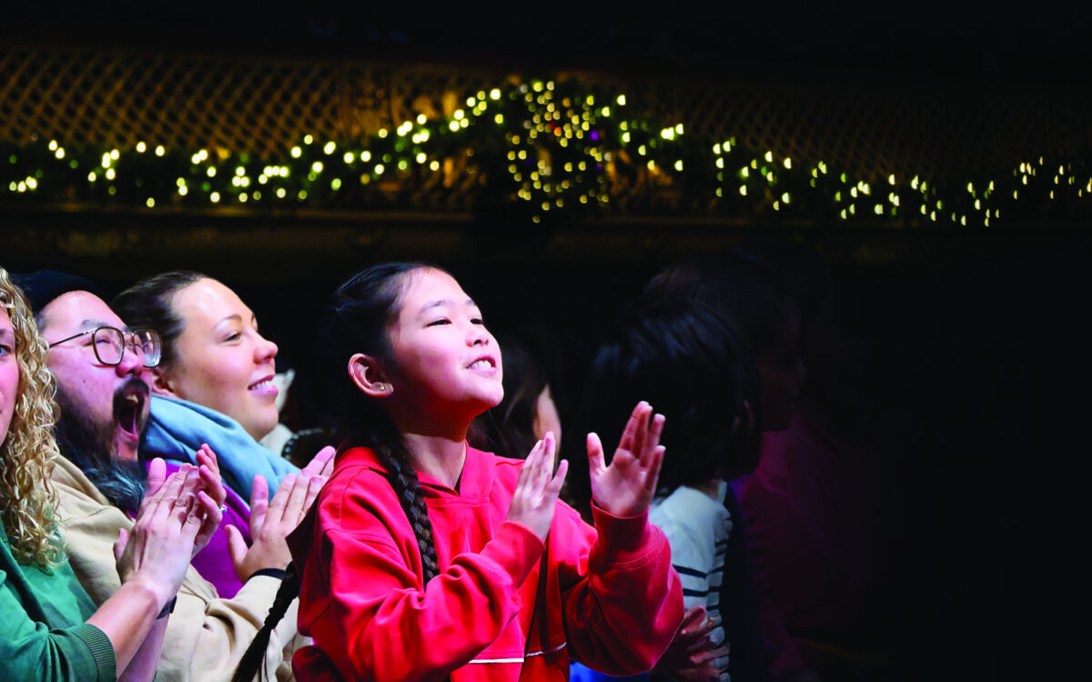 a young child smiles and applauds looking up at the stage