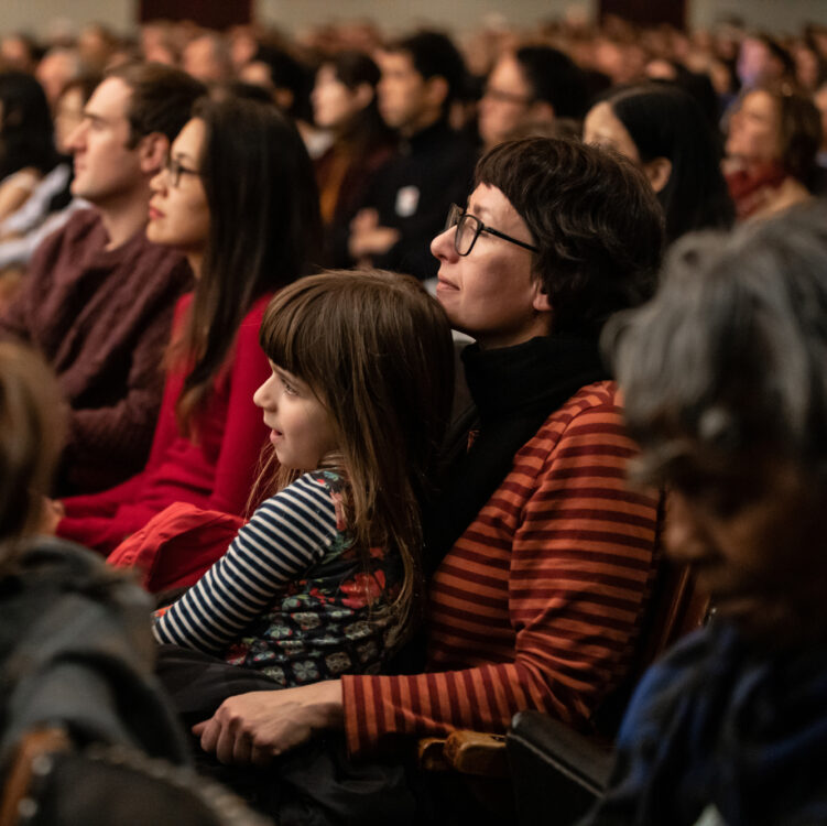 A young girl sit's on a woman's lap as they watch a BSO concert in Symphony Hall