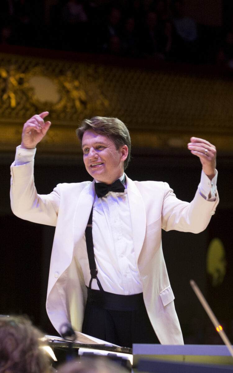 Boston Pops Conductor Keith Lockhart, wearing a white jacket, raises both hands to lead orchestra